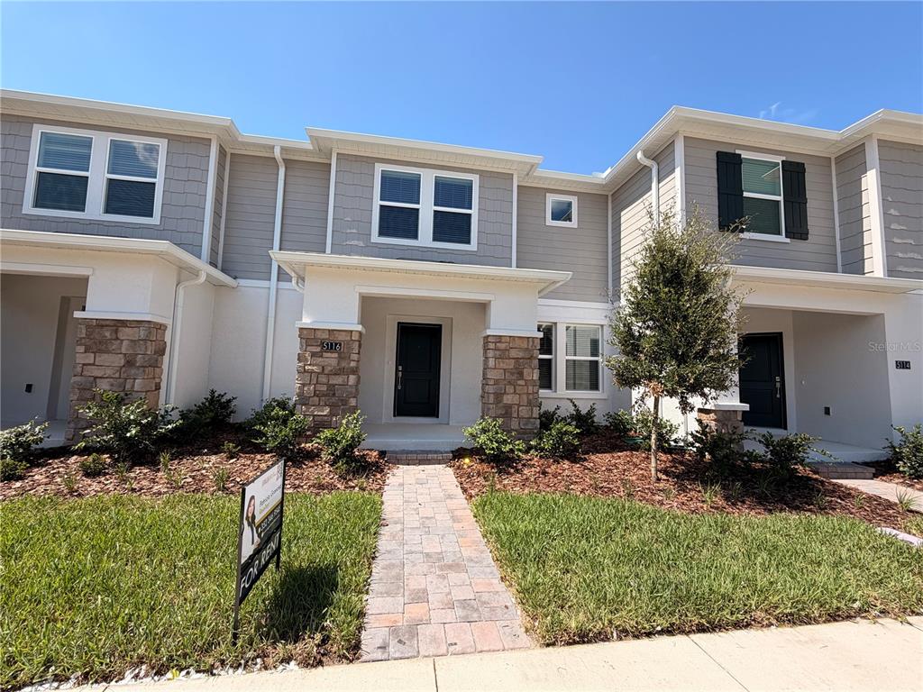 A two-story townhome exterior features light gray siding, stone accents, and a paved walkway — 5116 CLAY WHALEY ROAD, ST CLOUD, FL