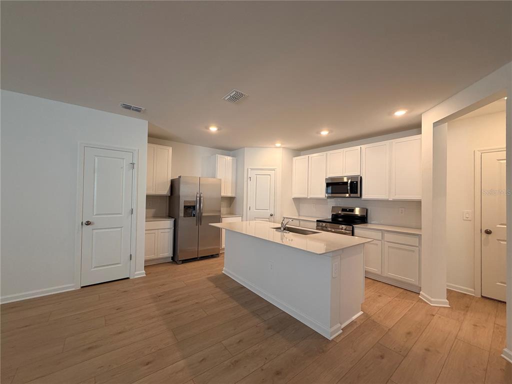 A kitchen features white cabinets, stainless steel appliances, a center island, and light wood flooring — 5116 CLAY WHALEY ROAD, ST CLOUD, FL