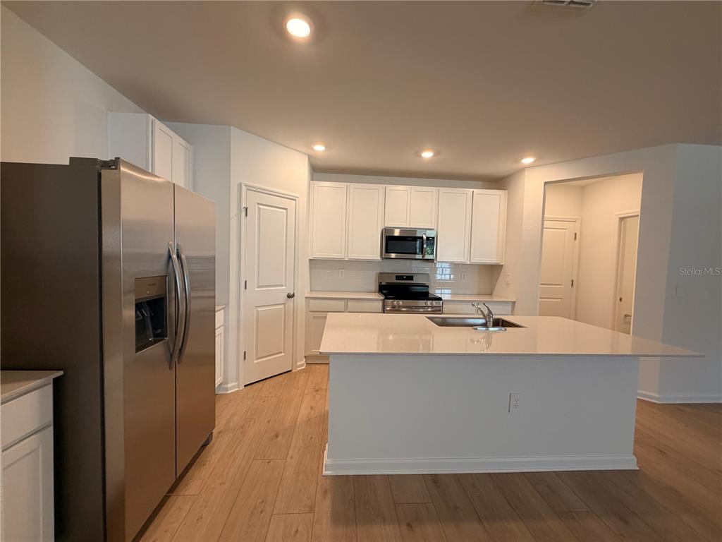 A kitchen features white cabinets, stainless steel appliances, a center island, and wood-look flooring — 5116 CLAY WHALEY ROAD, ST CLOUD, FL