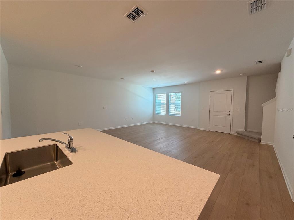 A kitchen island with a sink overlooks an open-concept living area with light wood flooring — 5116 CLAY WHALEY ROAD, ST CLOUD, FL