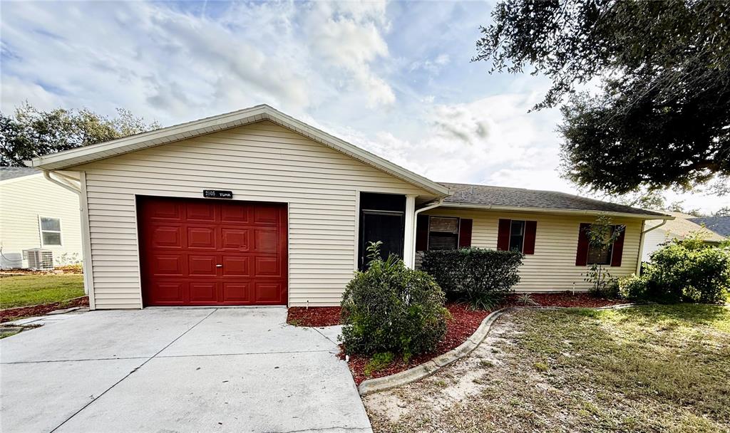 A single-story house with beige siding, a red garage door, and a concrete driveway — 2105 GREENLAW COURT UNIT 2105, LEESBURG, FL