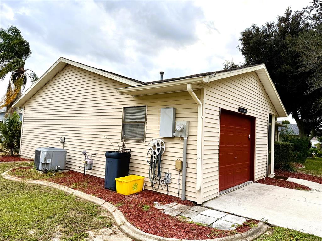 The exterior of a house features beige vinyl siding, a red garage door, and landscaping — 2105 GREENLAW COURT UNIT 2105, LEESBURG, FL