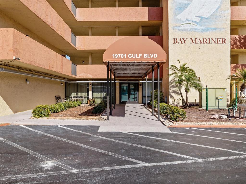 The exterior entrance of a multi-story building features a tan awning and a painted mural — 19701 GULF BOULEVARD UNIT 105, INDIAN SHORES, FL