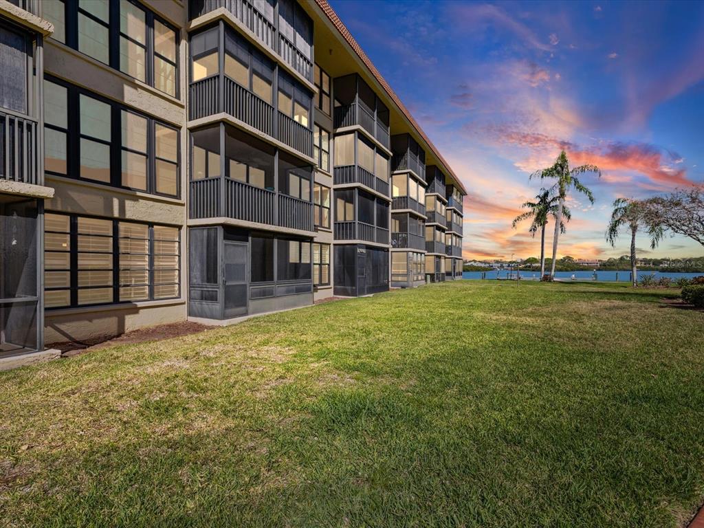 A multi-story apartment building with screened balconies sits next to a grassy lawn and water — 19701 GULF BOULEVARD UNIT 105, INDIAN SHORES, FL