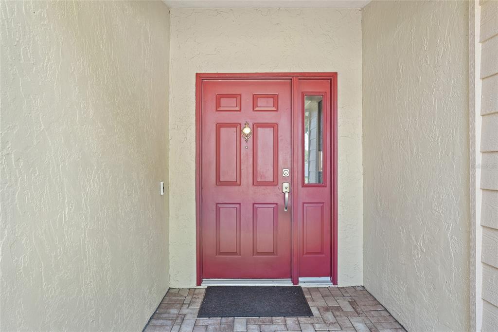 A red front door with a side window sits under a covered entryway — 665 ROSEMERE CIRCLE, ORLANDO, FL