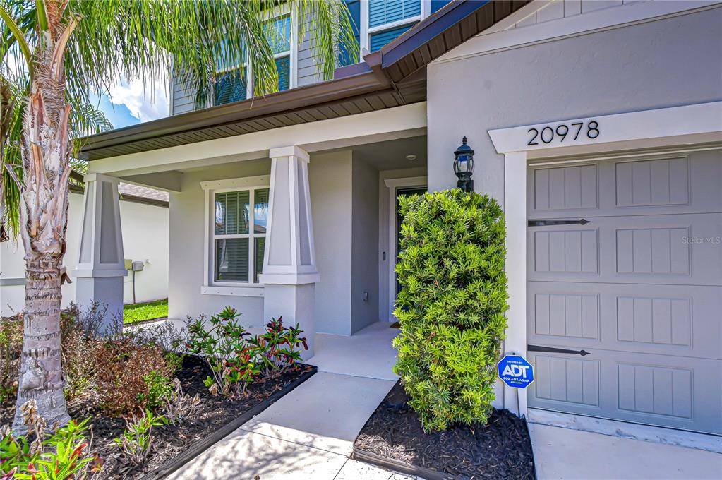 The exterior of a two-story house features a gray garage, a covered entryway, and landscaping — 20978 MONZA LOOP, LAND O LAKES, FL