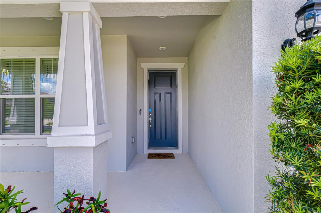 A covered entryway features a dark blue front door, a white column, and a doormat — 20978 MONZA LOOP, LAND O LAKES, FL