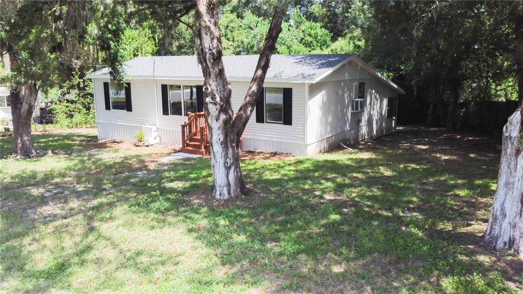 A single-story mobile home with white siding and black shutters sits on a wooded lot — 8017 E SKYLINE LANE, FLORAL CITY, FL