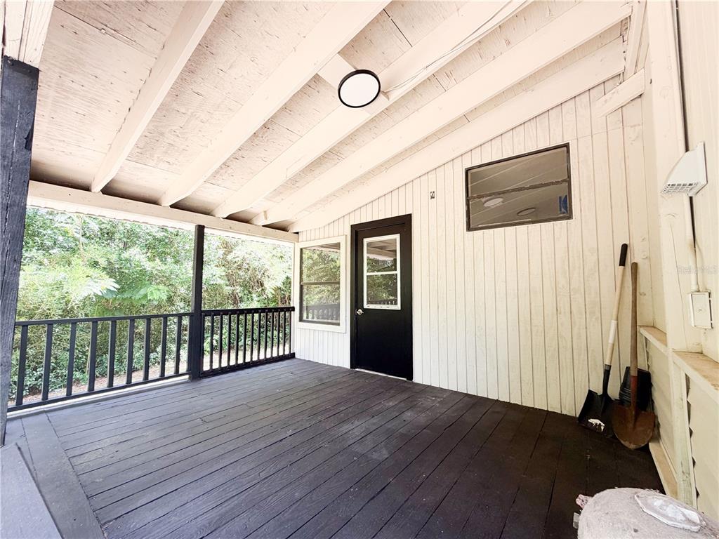 A covered wooden porch features a black door, white vertical siding, and a black railing — 8017 E SKYLINE LANE, FLORAL CITY, FL
