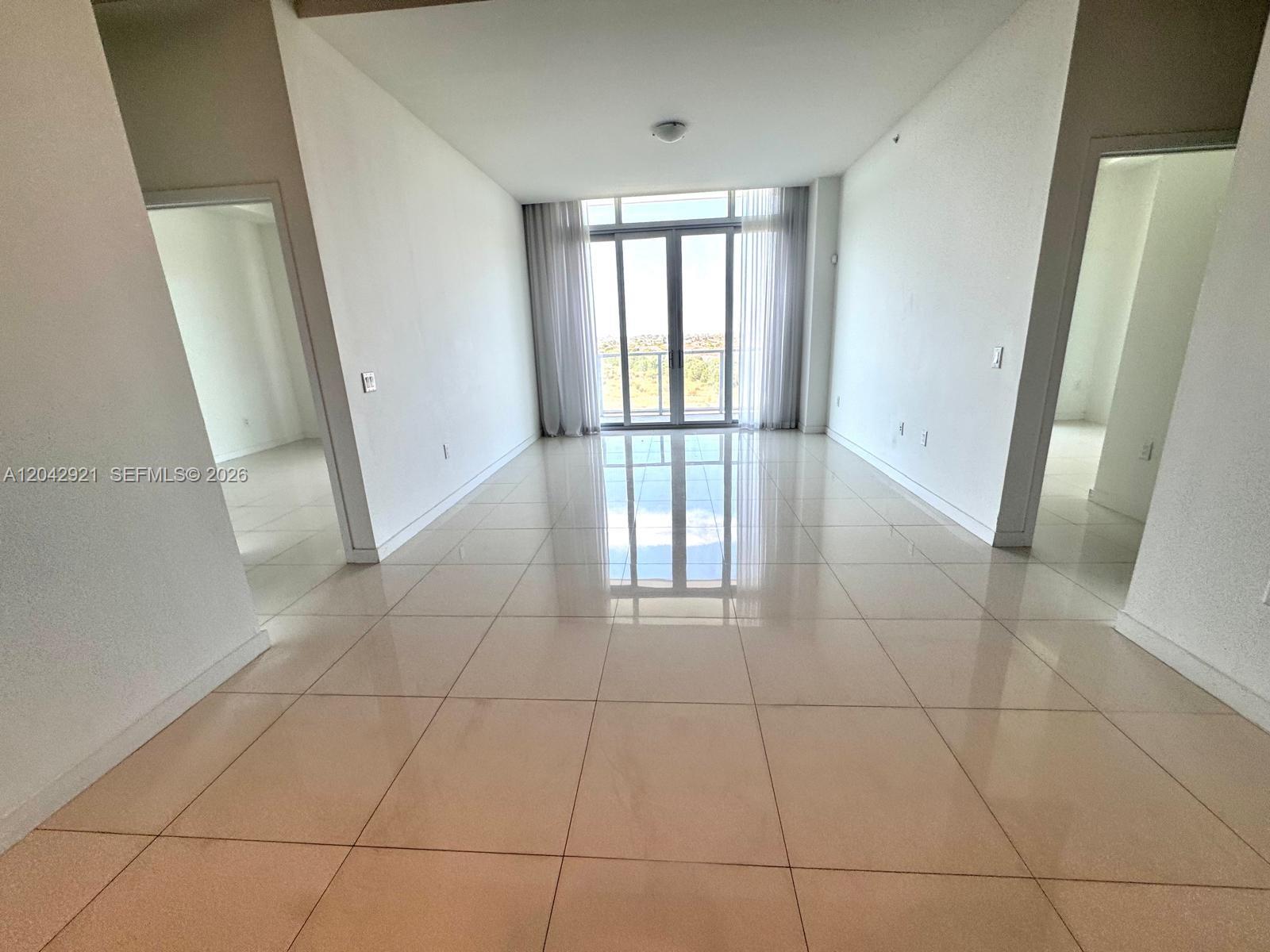 An empty room features white walls, large beige floor tiles, and a glass balcony door — 7825 NW 107th Ave # 706, Doral FL 33178, DORAL, FL