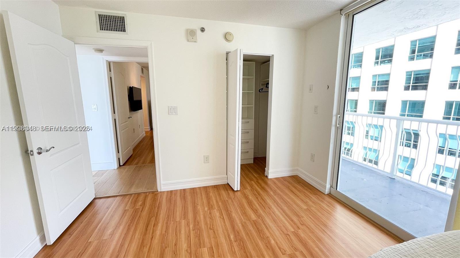 A bedroom features light wood-look flooring, a closet with shelving, and a sliding glass door — 1200 Brickell Bay Dr # 1702, Miami FL 33131, MIAMI, FL