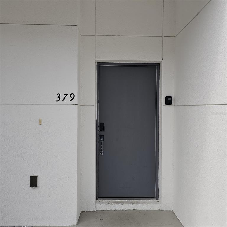 A gray front door with a smart lock is set into a white stucco exterior wall — 379 FAMAGUSTA DRIVE, DAVENPORT, FL