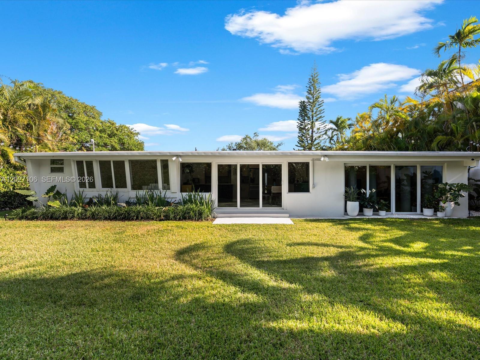 The exterior of a white, single-story house features large glass windows and sliding doors — 1945 Alamanda Dr # 0, North Miami FL 33181, NORTH MIAMI, FL