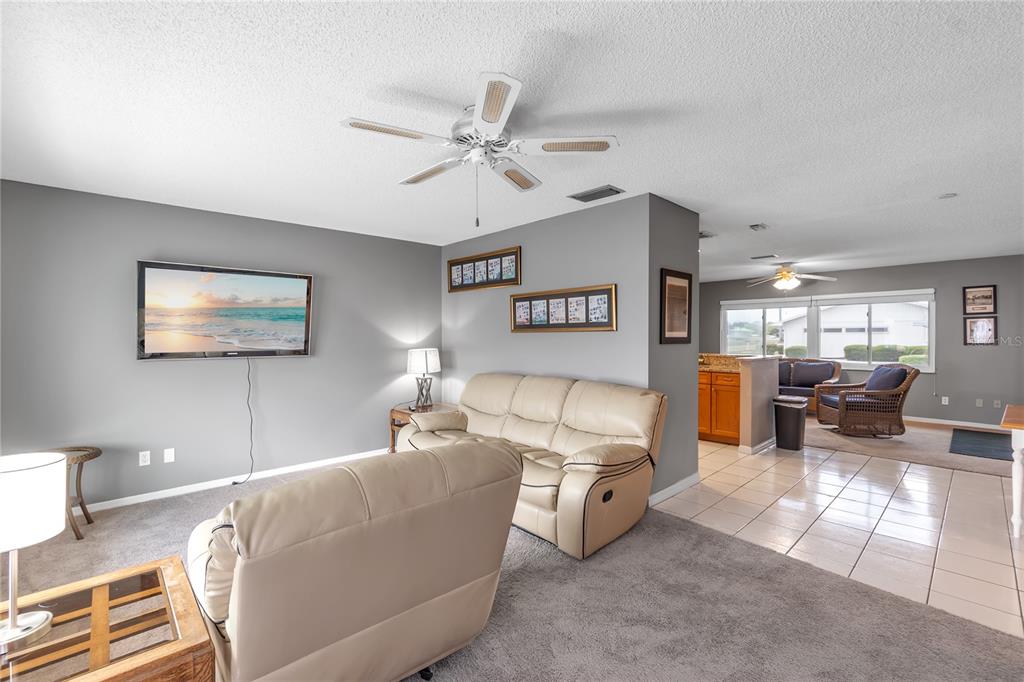 A living room with gray walls, beige leather furniture, and a view into a kitchen — 702 HUXLEY PLACE, SUN CITY CENTER, FL