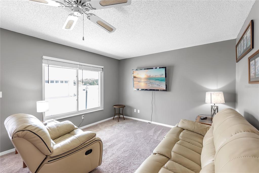 A living room features a beige sofa, a matching recliner, a wall-mounted television, and carpet — 702 HUXLEY PLACE, SUN CITY CENTER, FL