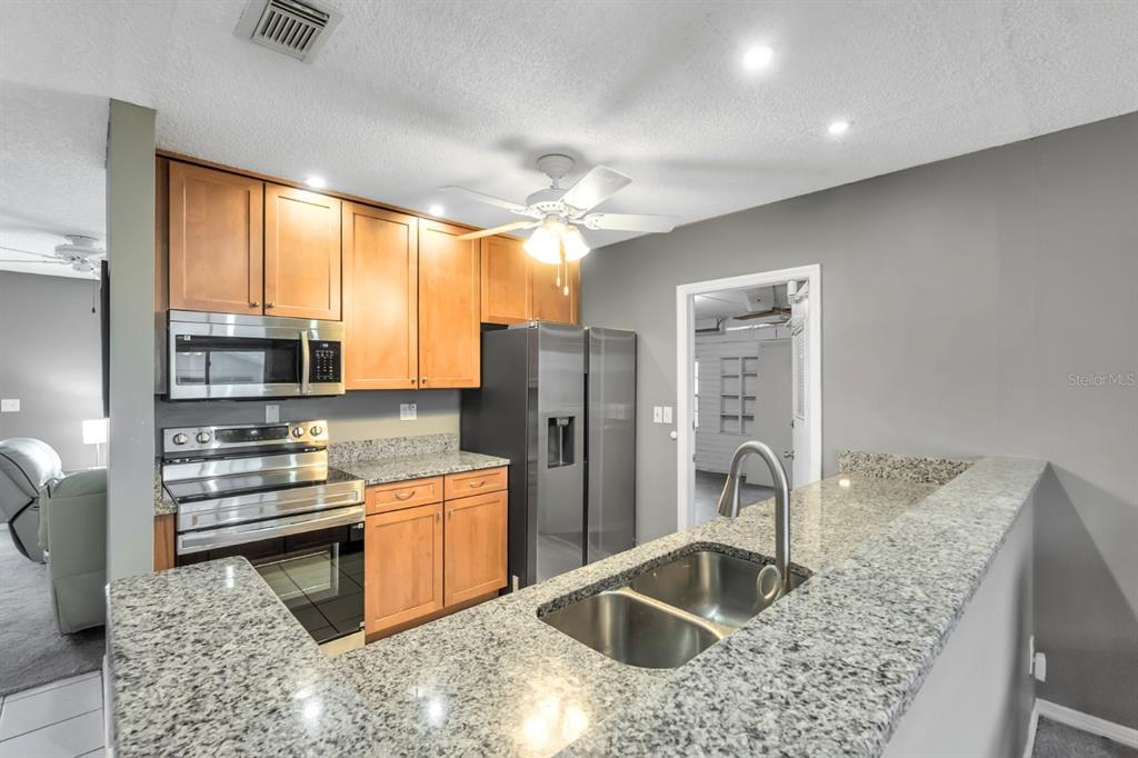 A kitchen with wood cabinets, stainless steel appliances, and a granite-topped peninsula with a sink — 702 HUXLEY PLACE, SUN CITY CENTER, FL