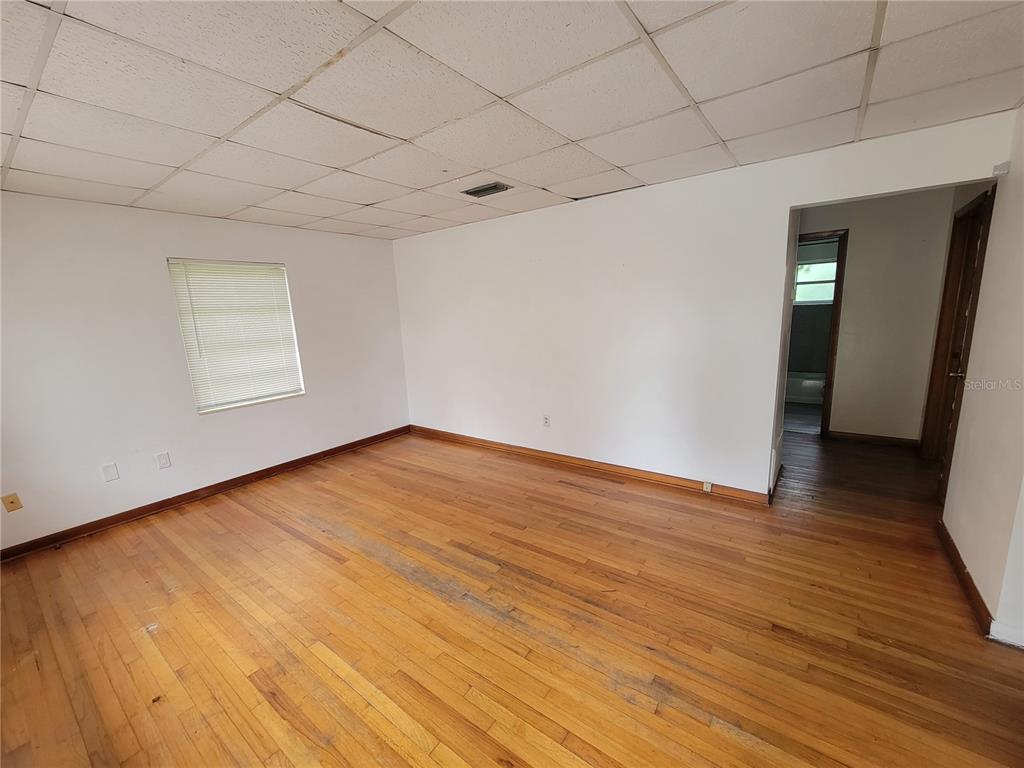 An empty room features hardwood floors, white walls, and a drop ceiling with a vent — 5939 SE HOLLY ROAD, BELLEVIEW, FL