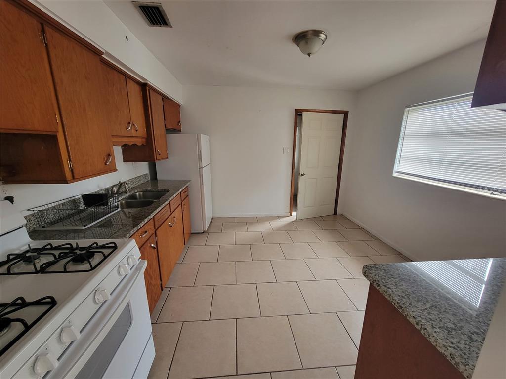 A kitchen features wood cabinets, granite countertops, a white stove, and light-colored floor tiles — 5939 SE HOLLY ROAD, BELLEVIEW, FL