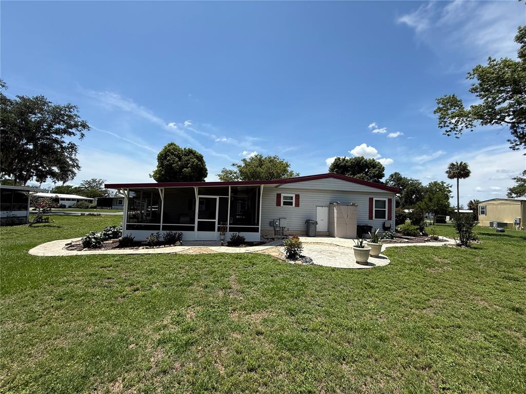A single-story mobile home features a screened-in porch and a paved patio area — 19 MAGNOLIA LANE, WILDWOOD, FL