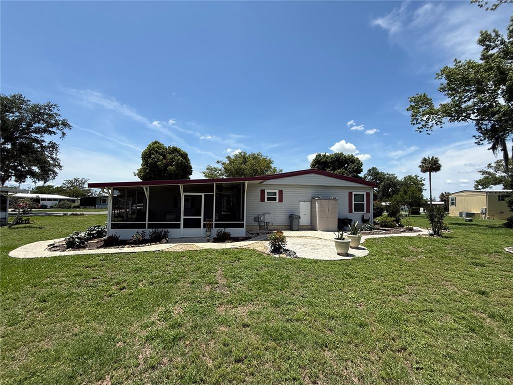 A single-story manufactured home features a screened-in porch, light siding, and a decorative concrete patio — 19 MAGNOLIA LANE, WILDWOOD, FL