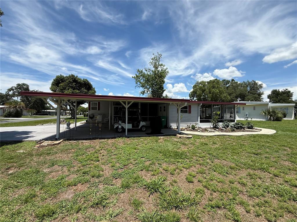 A single-story manufactured home with a large carport and a screened-in porch — 19 MAGNOLIA LANE, WILDWOOD, FL