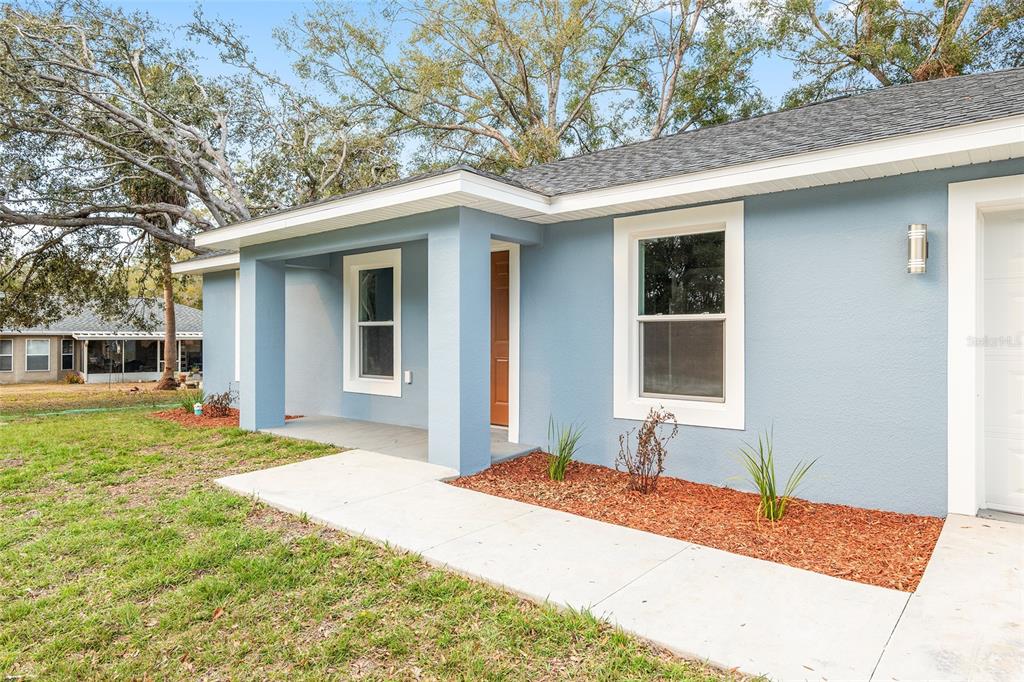 A light blue house exterior features a covered front porch, a concrete walkway, and landscaping — 24743 NW HIGHVIEW AVENUE, DUNNELLON, FL