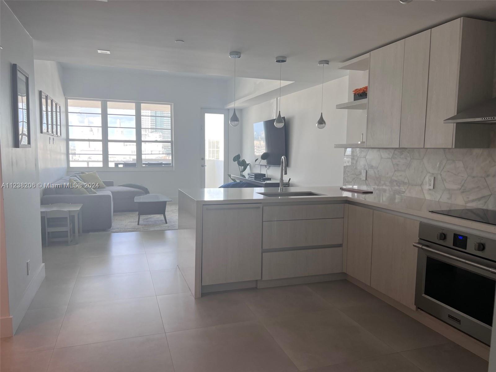 A modern kitchen with light wood cabinets and a stone island overlooks a living area — 100 Lincoln Rd # 1608, Miami Beach FL 33139, MIAMI BEACH, FL