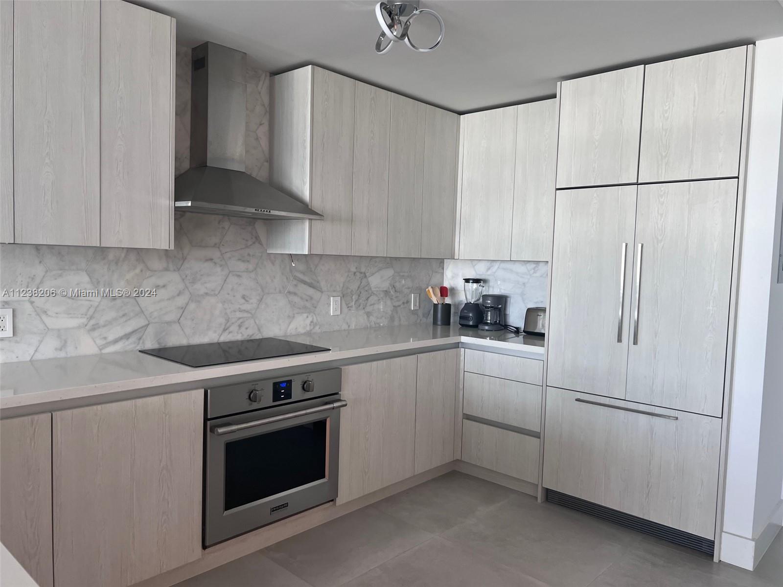 A modern kitchen features light wood-grain cabinets, stainless steel appliances, and a marble hexagonal backsplash — 100 Lincoln Rd # 1608, Miami Beach FL 33139, MIAMI BEACH, FL