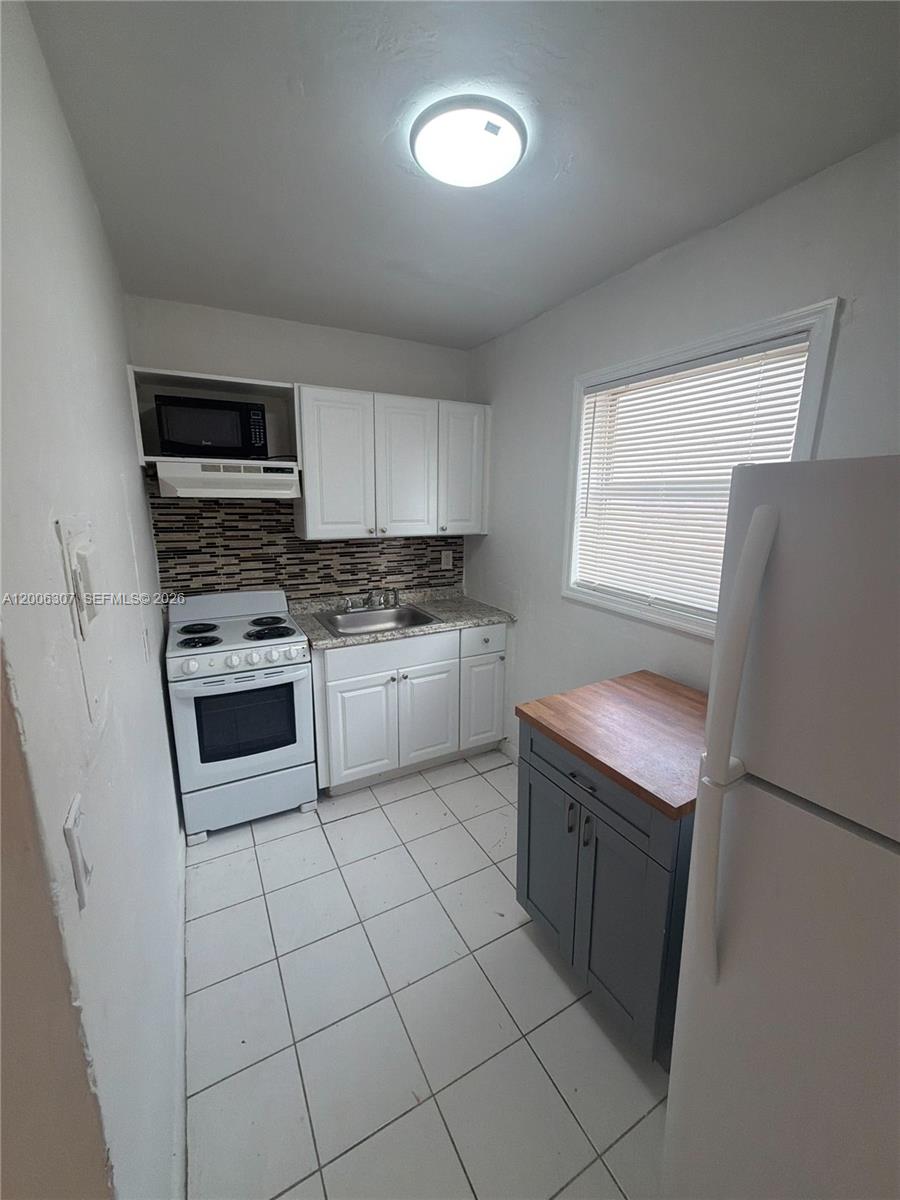 A small kitchen features white cabinets, a white stove, a grey island, and tiled floors — 3669 Thomas Ave # 10, Miami FL 33133, MIAMI, FL