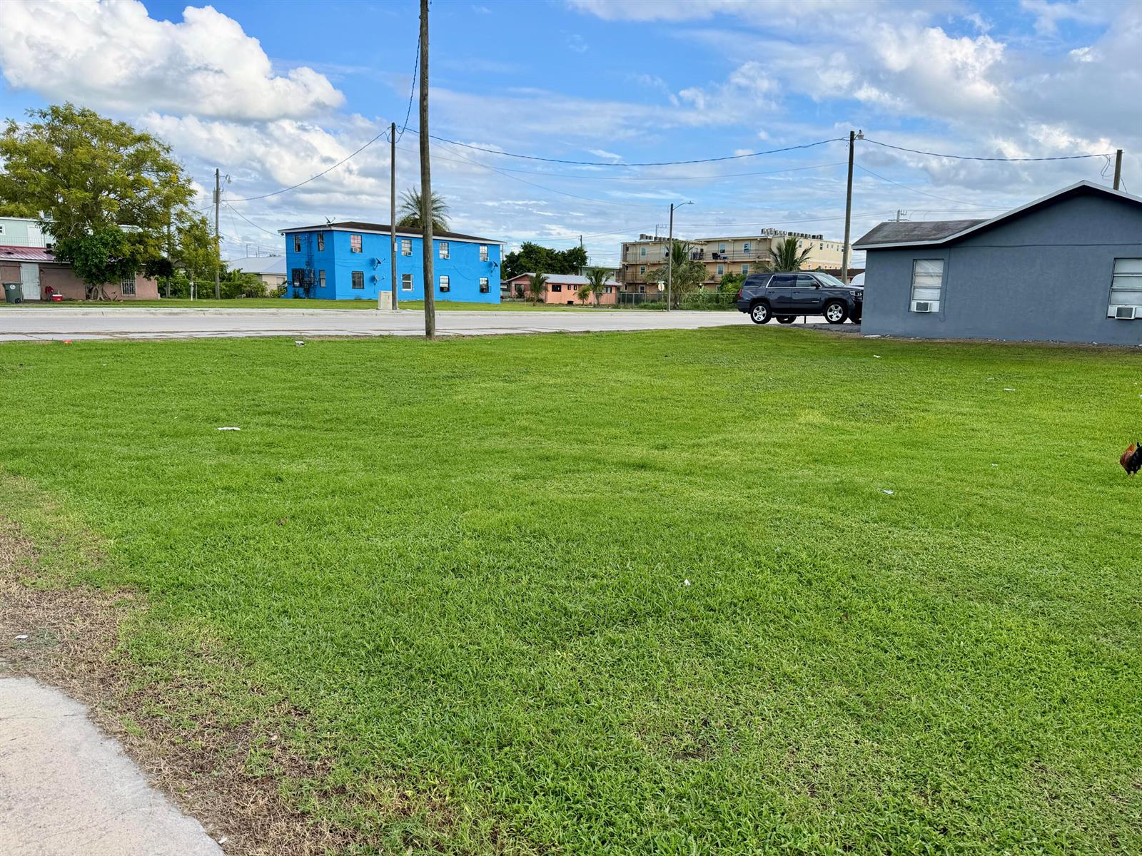 A large, grassy vacant lot sits in front of a blue building and a house — 348 SW 8th Street, Belle Glade FL 33430, BELLE GLADE, FL