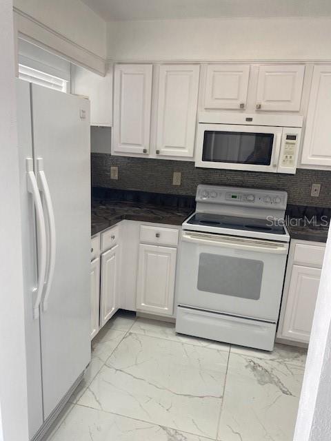 A kitchen features white cabinets, white appliances, dark countertops, and light-colored marble-patterned tile flooring — 1820 Amberly Avenue # 10, Orlando FL 32822, ORLANDO, FL