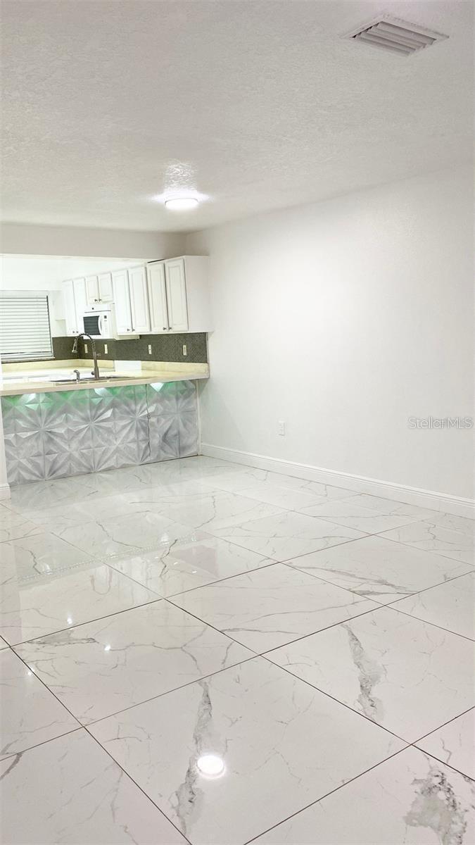 A kitchen with white cabinets and a geometric-patterned island overlooks a tiled dining area — 1820 Amberly Avenue # 10, Orlando FL 32822, ORLANDO, FL