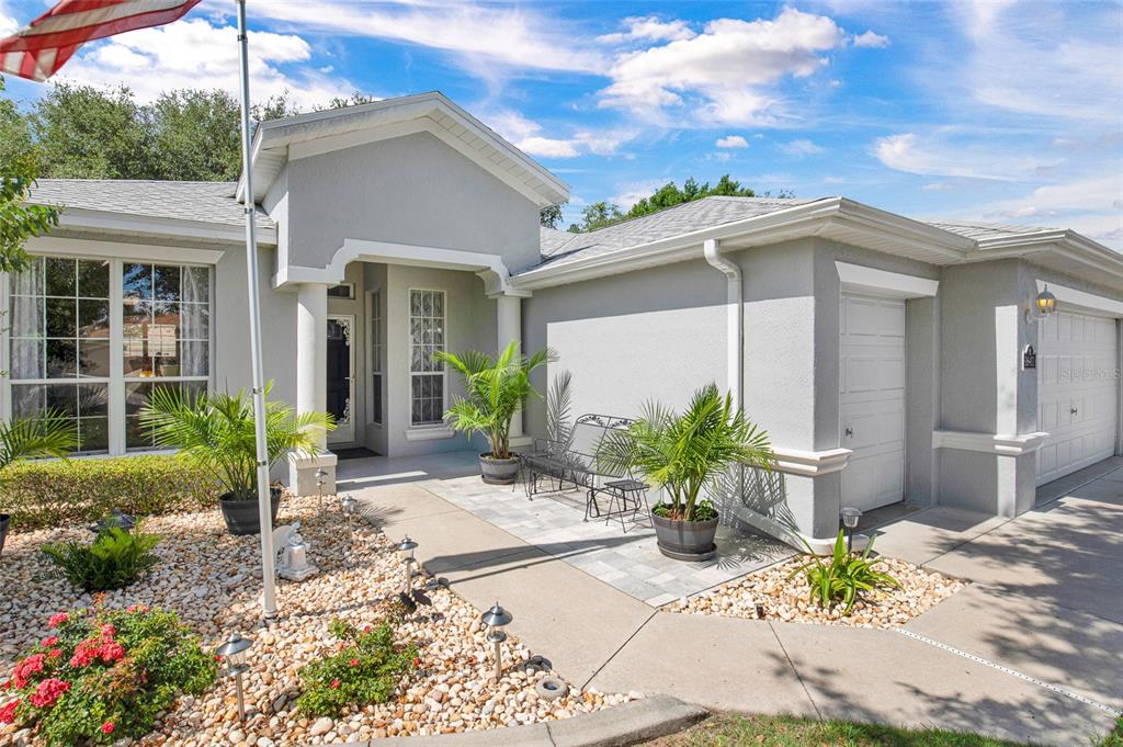 A gray single-story house features a paved entryway, potted palm plants, and a gravel garden — 16411 SW 14TH AVENUE ROAD, OCALA, FL