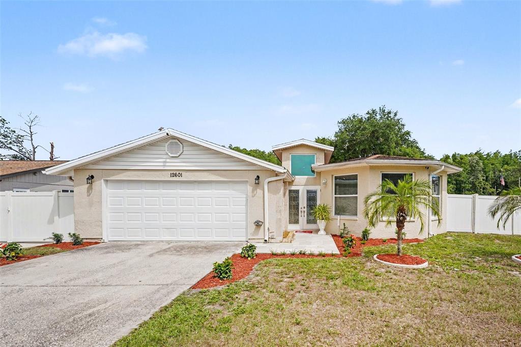 A single-story house with a white garage, beige stucco exterior, and a front palm tree — 12601 WOOD IBIS WAY, TAMPA, FL