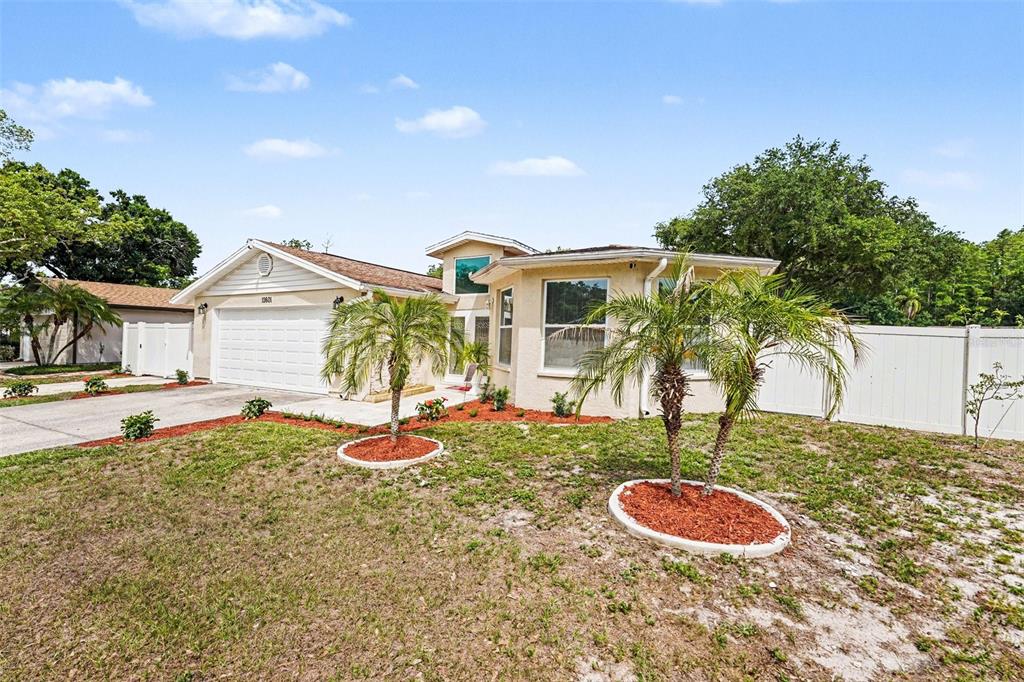 A single-story house with a white garage, beige stucco exterior, and two small palm trees — 12601 WOOD IBIS WAY, TAMPA, FL
