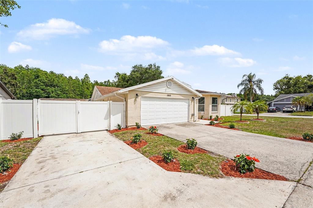 A single-story house with a white garage door, concrete driveway, and a white privacy fence — 12601 WOOD IBIS WAY, TAMPA, FL