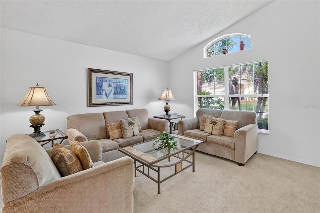 A living room features beige sofas, a glass-top coffee table, and an arched window — 1255 SEASONS BOULEVARD, KISSIMMEE, FL