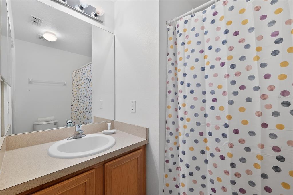 A bathroom features a wooden vanity with a beige countertop, a mirror, and a polka-dot curtain — 1255 SEASONS BOULEVARD, KISSIMMEE, FL