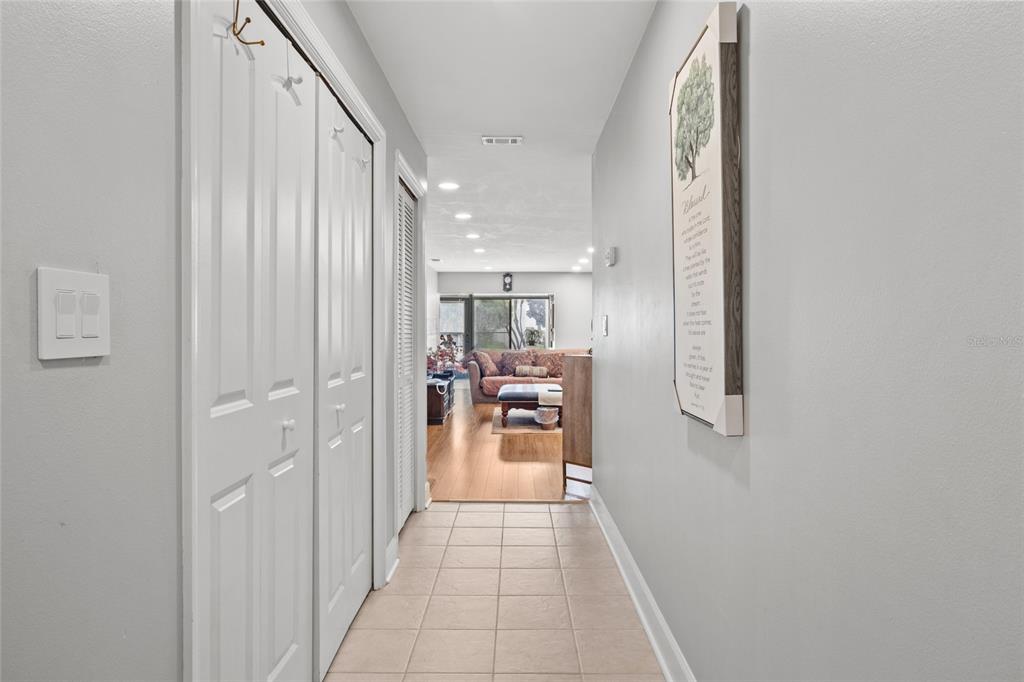 A tiled hallway leads from a white-doored closet toward a living room with hardwood floors — 13140 VILLAGE CHASE CIRCLE UNIT 13140, TAMPA, FL