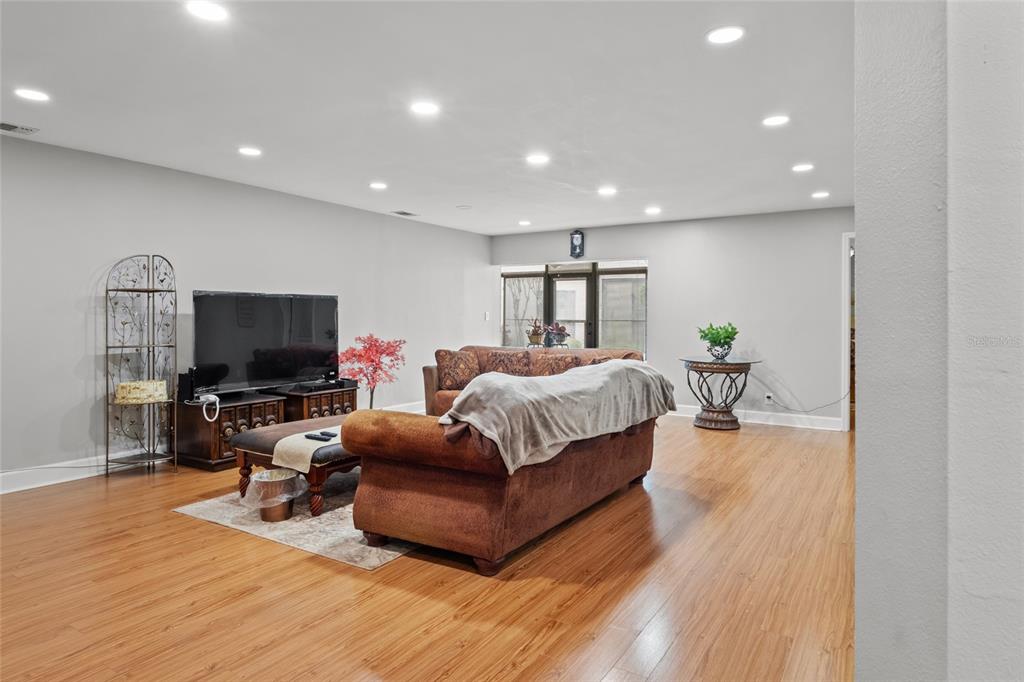 A living room features wood-look flooring, recessed lighting, a television, and brown upholstered furniture — 13140 VILLAGE CHASE CIRCLE UNIT 13140, TAMPA, FL