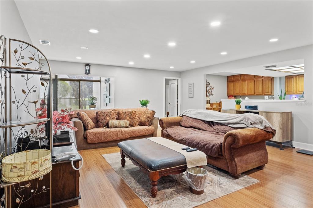 A living room with wood flooring, two sofas, a leather ottoman, and an open kitchen — 13140 VILLAGE CHASE CIRCLE UNIT 13140, TAMPA, FL