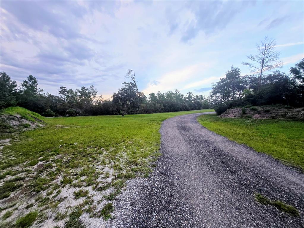 A gravel driveway leads through a grassy, wooded lot under a cloudy sky — 3130 LORI COURT, DELTONA, FL