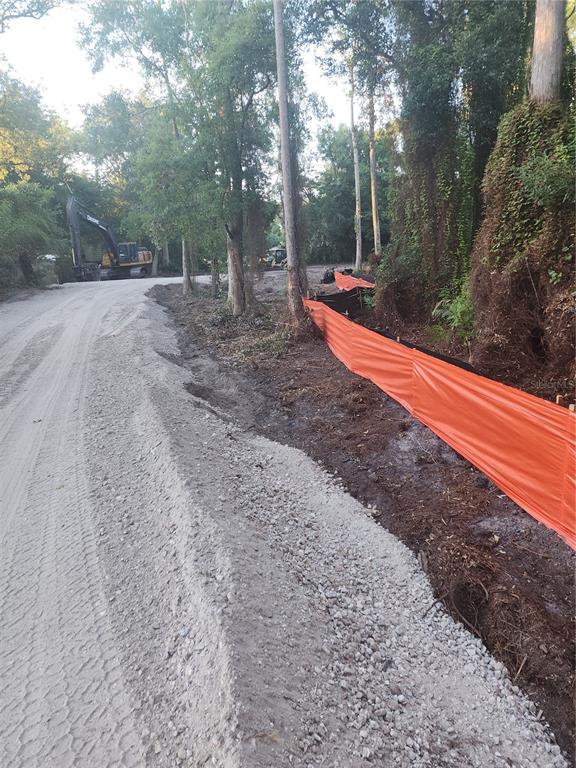 A dirt road runs alongside a wooded area with orange silt fencing and construction equipment — 7709 WINDWARD WAY, ODESSA, FL
