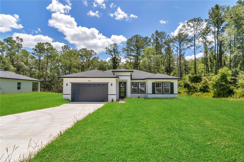 A single-story house with a dark garage door and white exterior sits on a lawn — 225 E CALDWELL DRIVE, DUNNELLON, FL