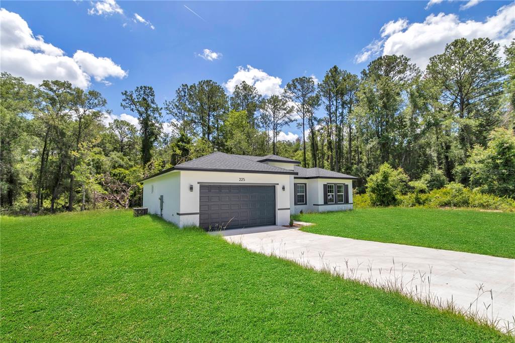A single-story white house with a dark garage door sits on a grassy lot — 225 E CALDWELL DRIVE, DUNNELLON, FL