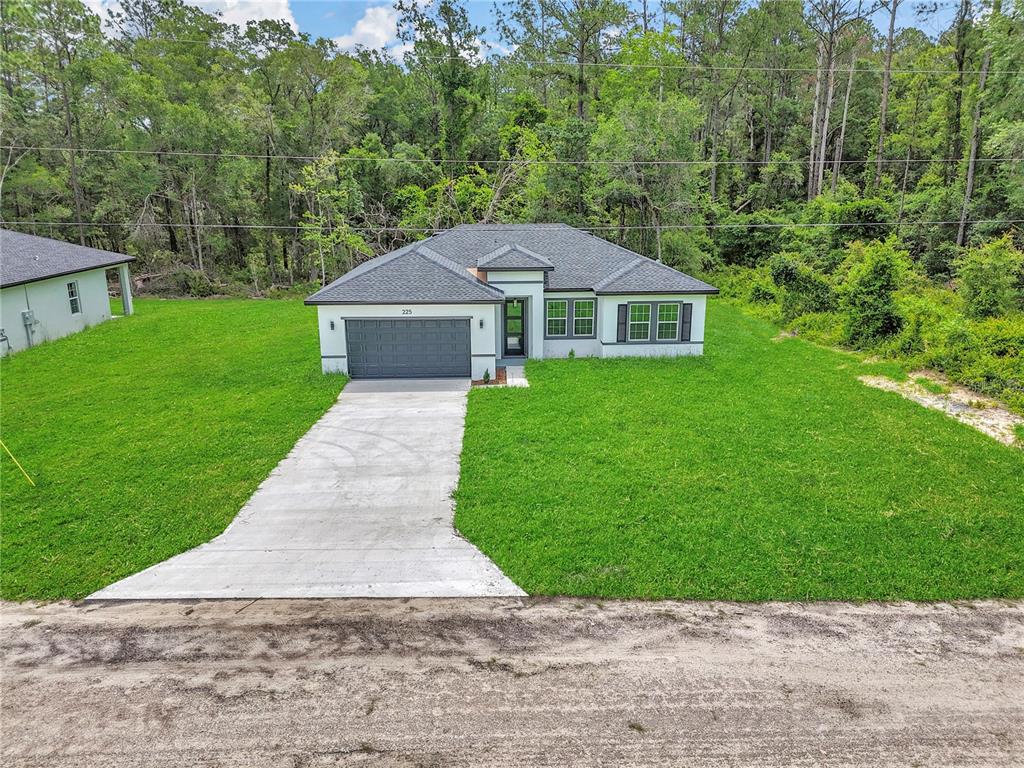 A single-story house with a gray garage and driveway sits on a grassy lot — 225 E CALDWELL DRIVE, DUNNELLON, FL