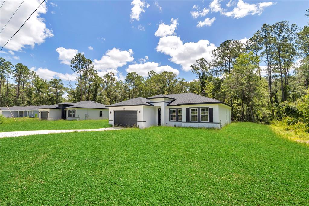 A modern, single-story white house with a dark garage and roof sits on a lawn — 225 E CALDWELL DRIVE, DUNNELLON, FL