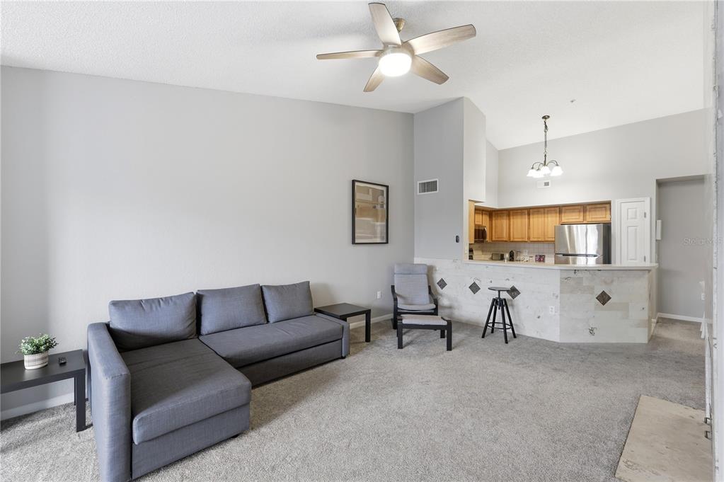 A living room with gray carpet, a sectional sofa, and a kitchen with a breakfast bar — 13001 MULBERRY PARK DRIVE UNIT 132, ORLANDO, FL