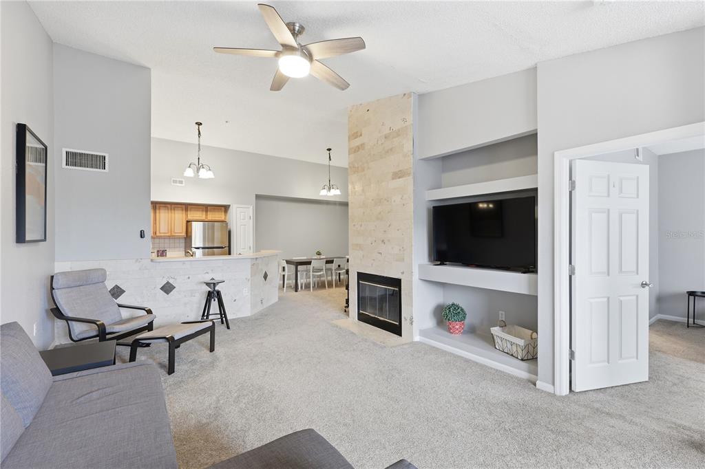 A living room features a stone fireplace, built-in shelving, a ceiling fan, and carpeted floors — 13001 MULBERRY PARK DRIVE UNIT 132, ORLANDO, FL