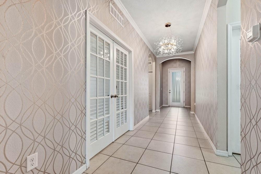A hallway features patterned wallpaper, tile flooring, a chandelier, French doors, and a console table — 1494 CHELSEA MANOR CIRCLE, DELAND, FL